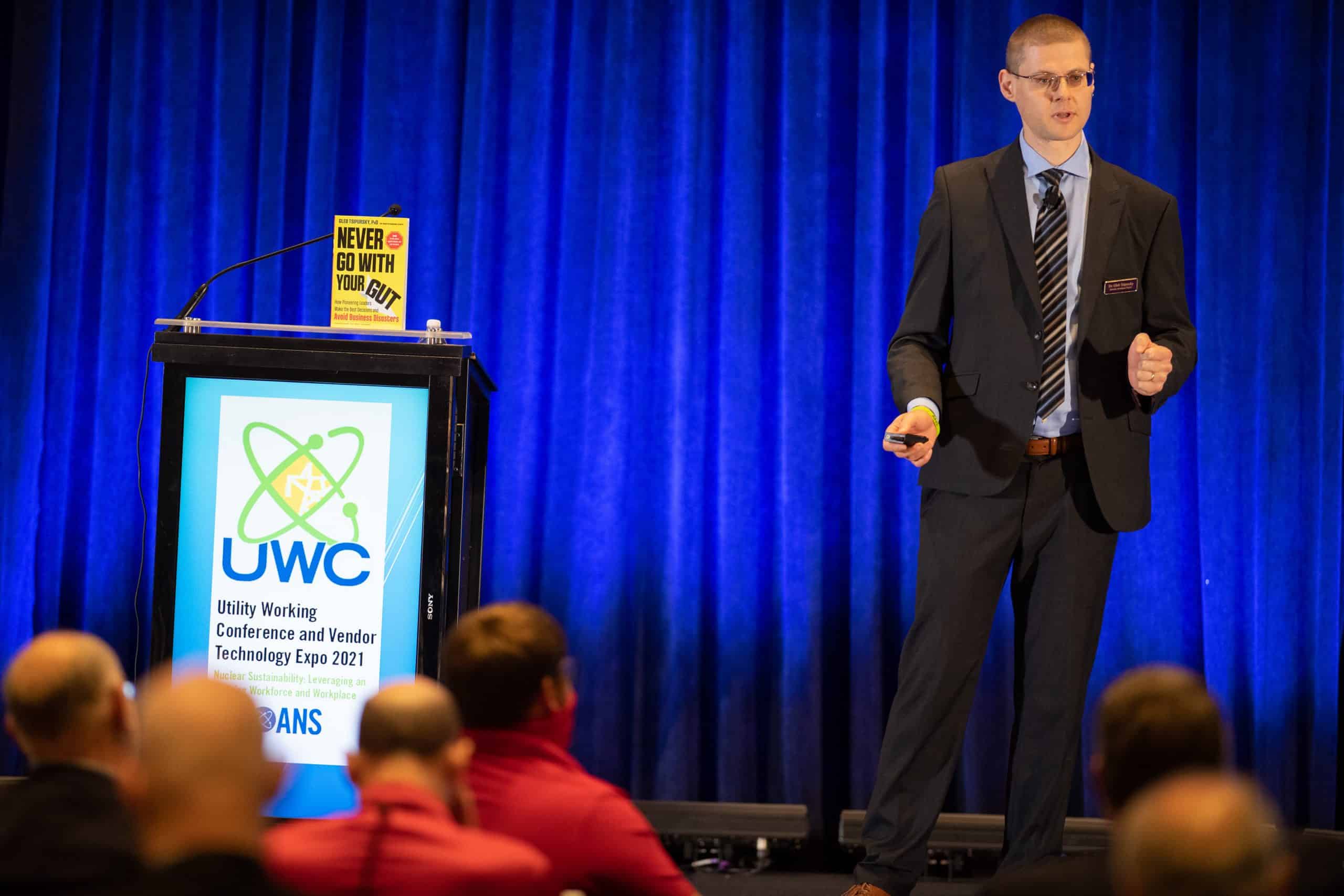 photo of Dr. Gleb speaking on a stage next to a copy of his book Never Go With Your Gut